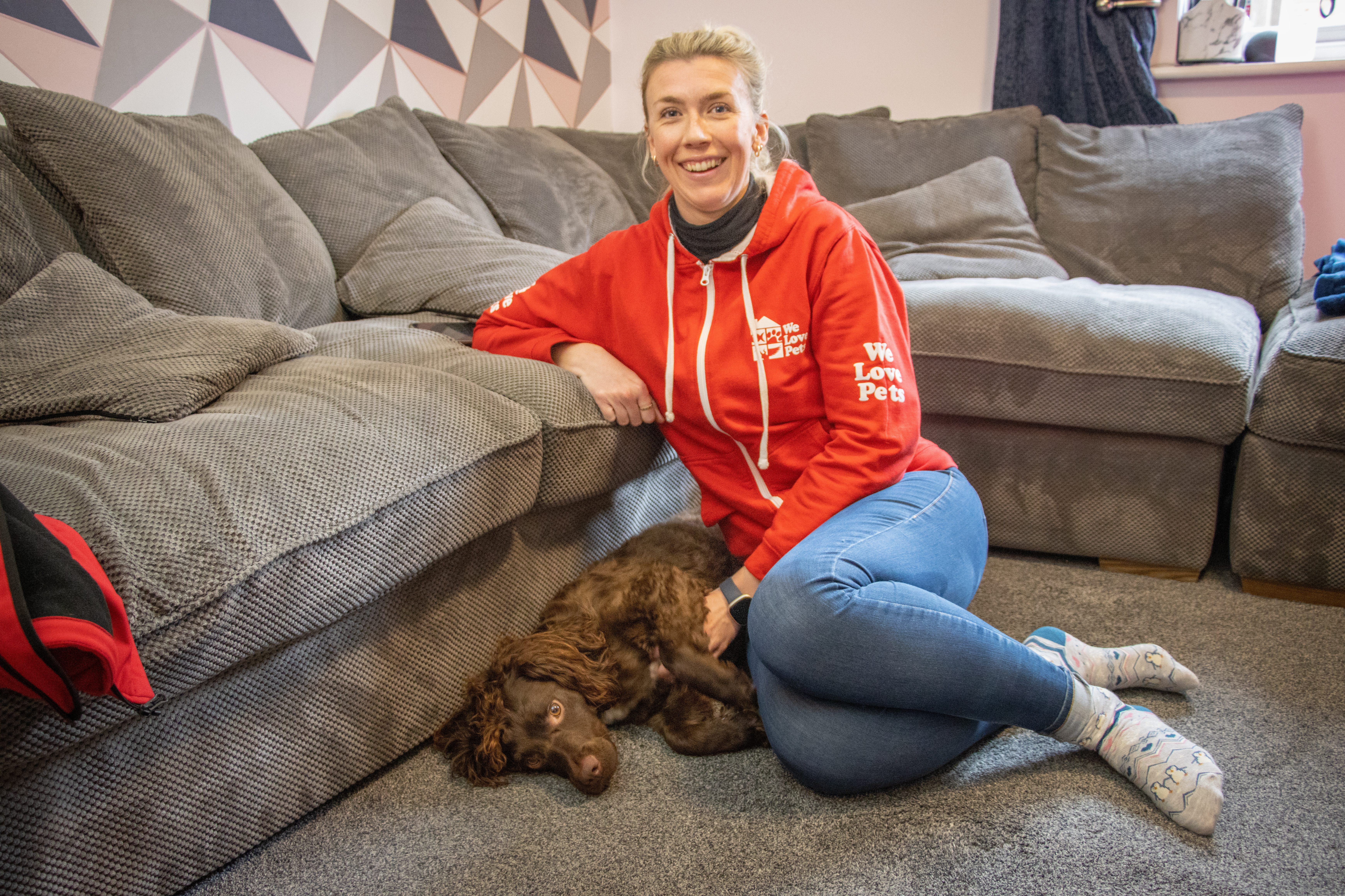 Kathryn of We Love Pets Burgess Hill sitting next to a grey sofa with a brown spaniel